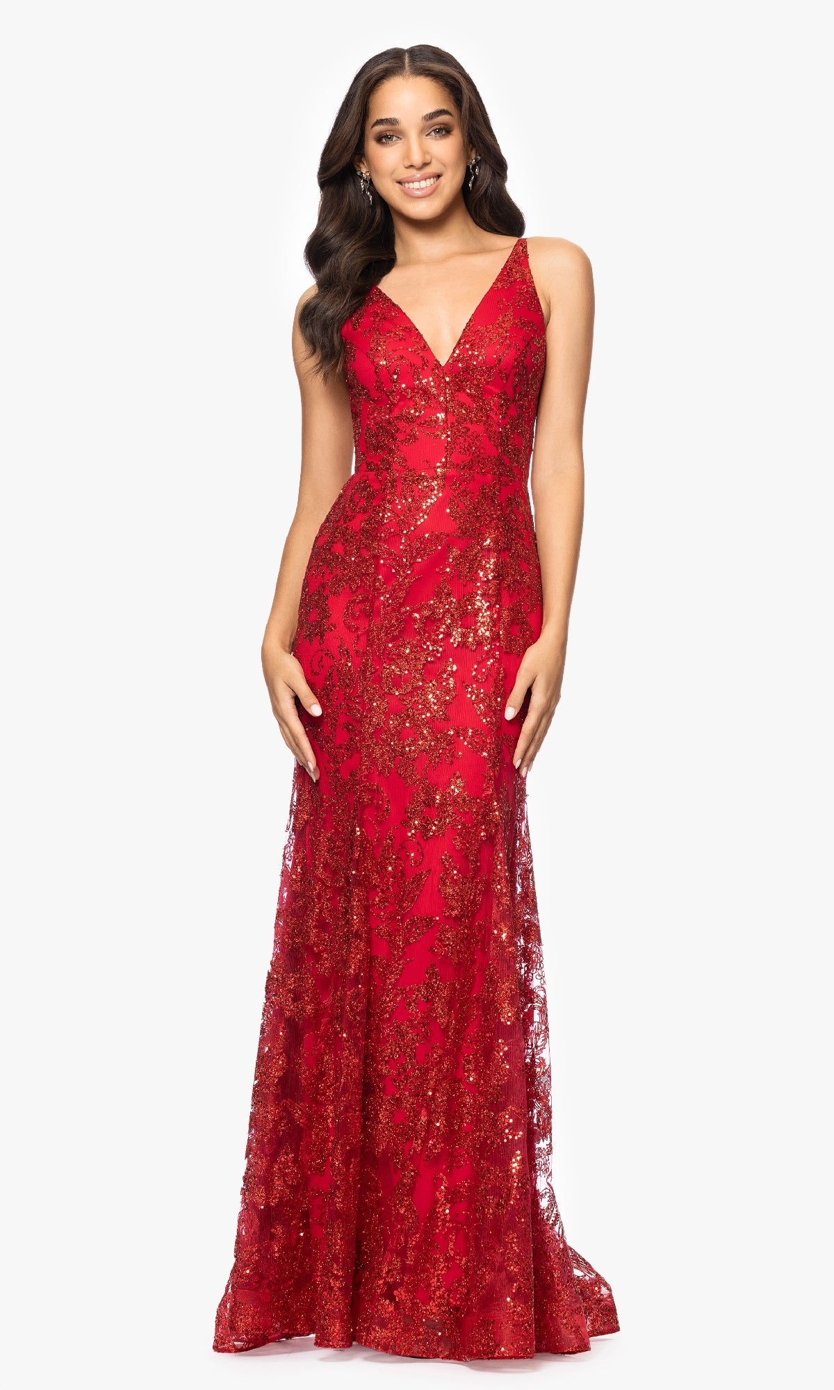 A woman smiles at the camera in front of a white background, wearing the Blondie Nites 4501BN—a red, floor-length prom dress with a strappy back, V-neckline, and gold sequin detailing.